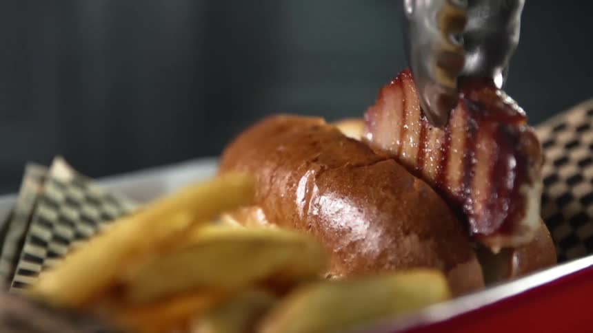 Grilled juicy steak is being placed between a bun