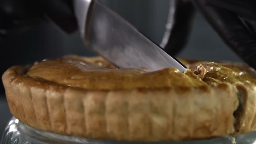 A person wearing black gloves slices a pie in half with a knife