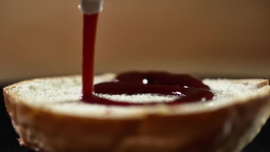 Ketchup squirting on the bottom half of a hamburger bun