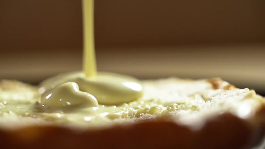 Bottom half of a hamburger bun being poured with mayonnaise