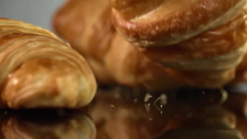 A trio of croissants are dropped down onto a highly reflective surface where they bounce around before coming to a rest