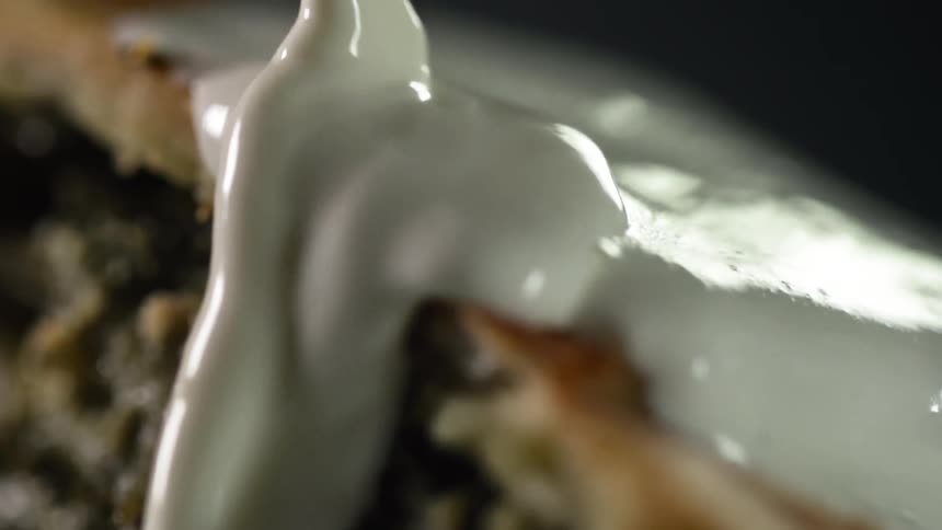 A white sauce pours over a meat dish