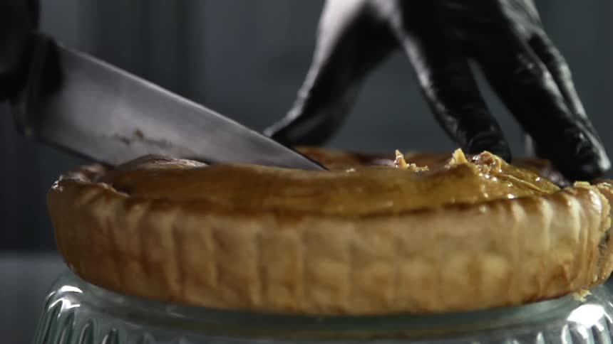 Chef wearing black latex gloves cuts a pie with a sharp kitchen knife
