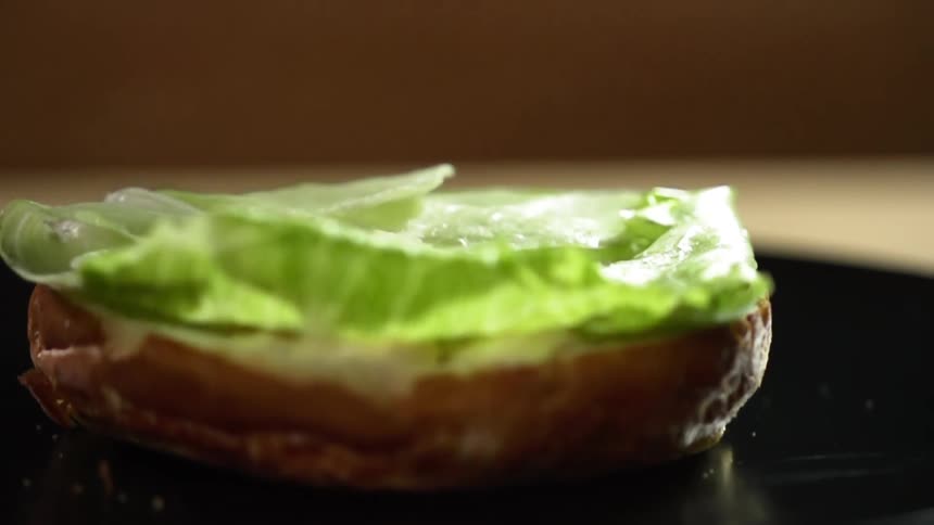 A piece of lettuce drops on a sauce covered burger bun