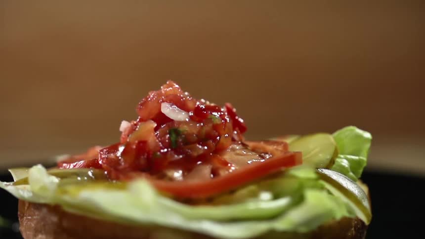 Salsa is dropped on top of a bun with lettuce pickles and tomatoes