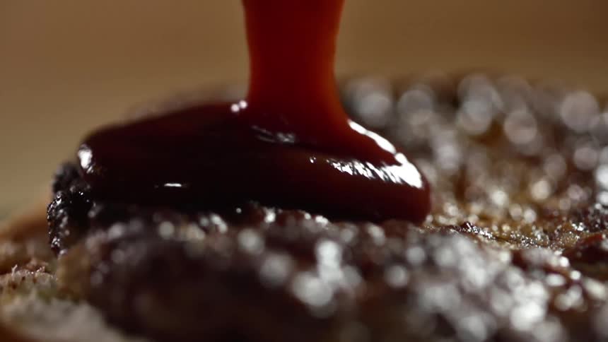 Ketchup pours over a burger patty