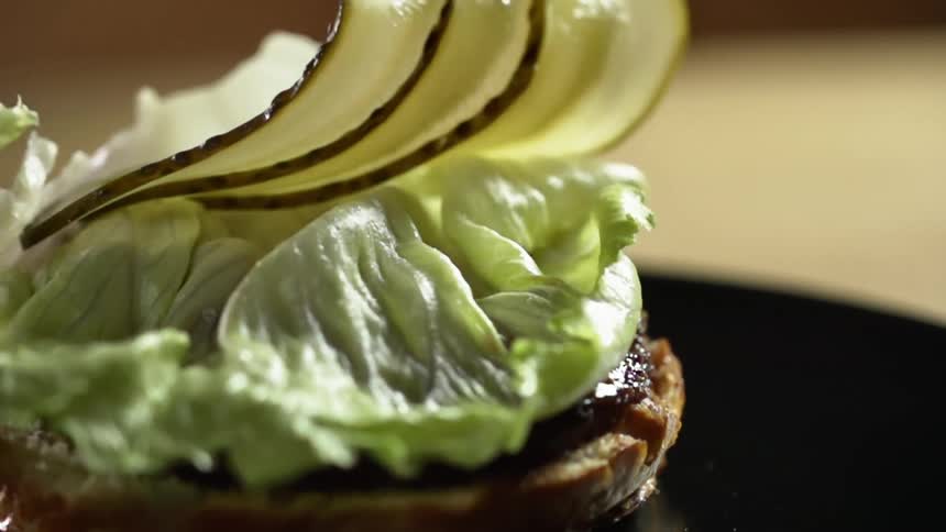 Pickle slices drop on a piece of lettuce sitting on a burger