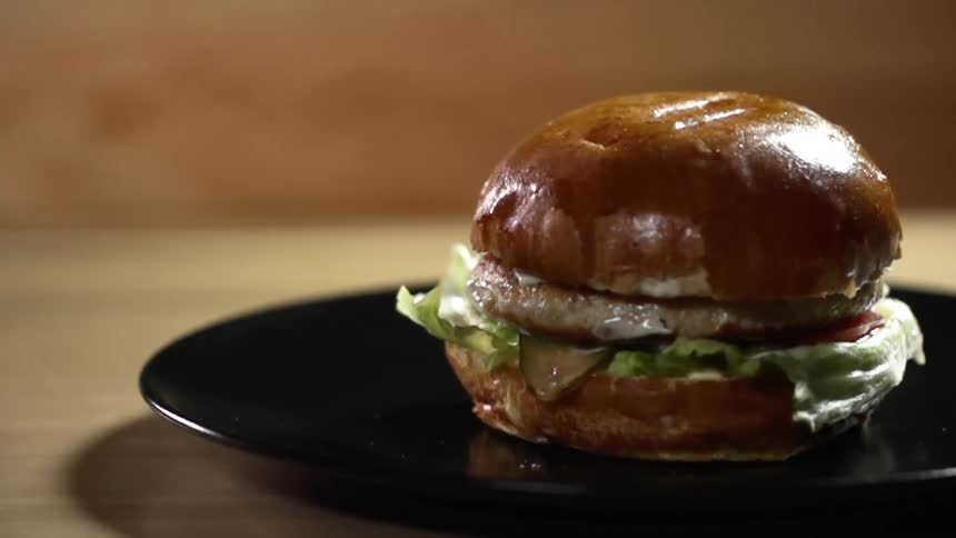 A bun top falls on a burger patty covered with sauce