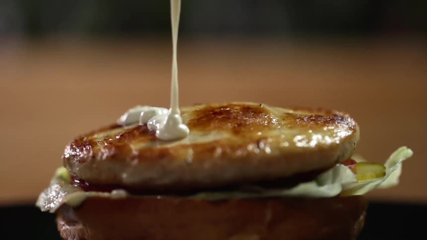Mayonnaise pouring on a chicken patty sitting on a bun
