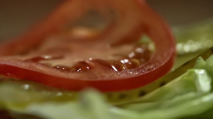 Slice of fresh red tomato falls over slices of pickle over lettuce