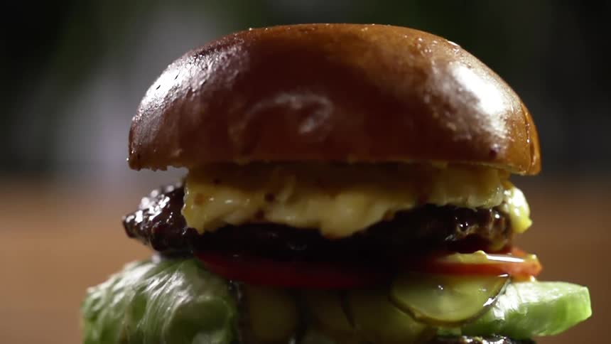 Top of a hamburger bun falls onto a prepared hamburger