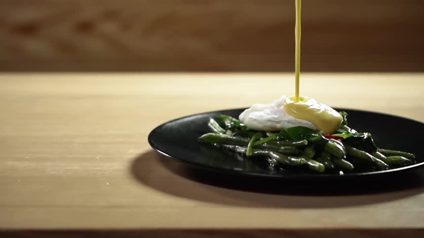 Mayonnaise is drizzled onto a plate of asparagus and a poached egg on a wooden table