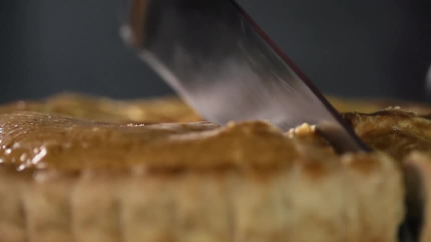 Chef wearing black latex gloves cuts a pie with a sharp kitchen knife