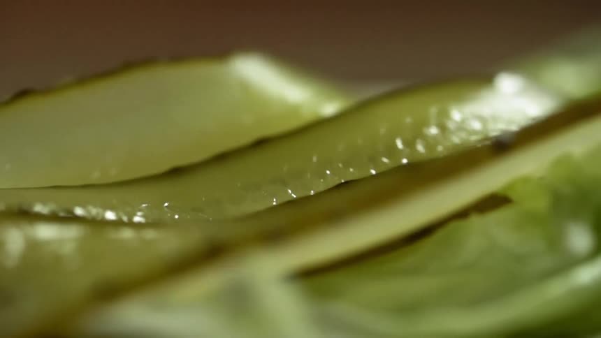 Long slices of pickles fall atop a slice of lettuce