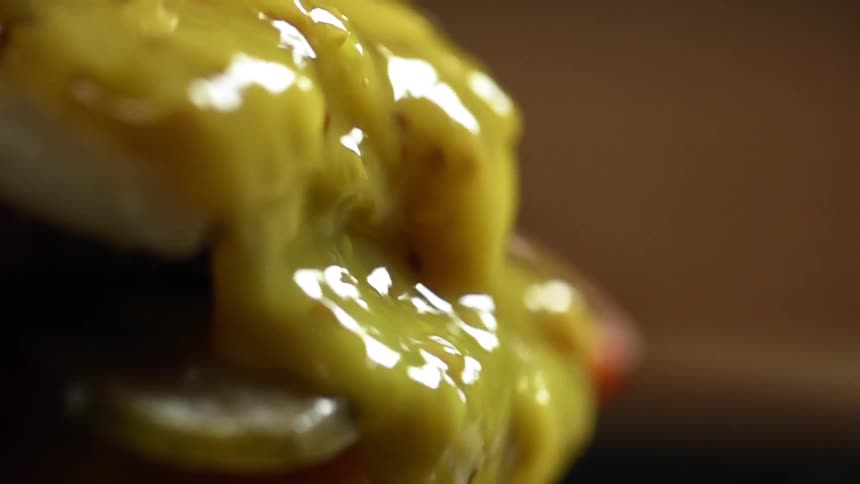Yellow sauce flowing over sliced tomatoes and pickles in a hamburger