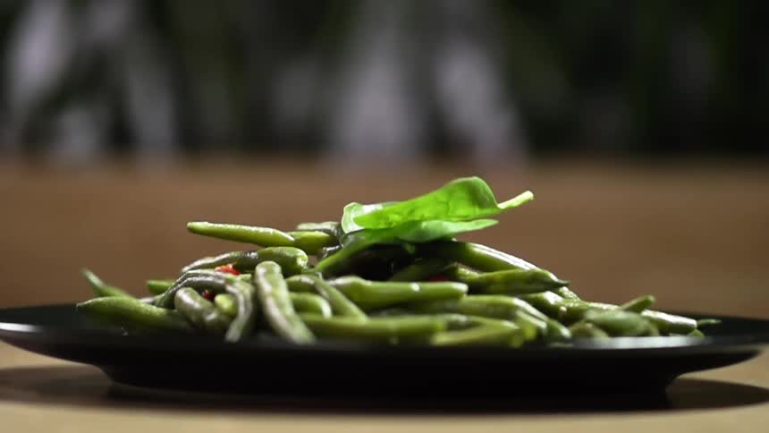 A plate containing a pile of cooked asparagus is topped with a few leaves of spinach