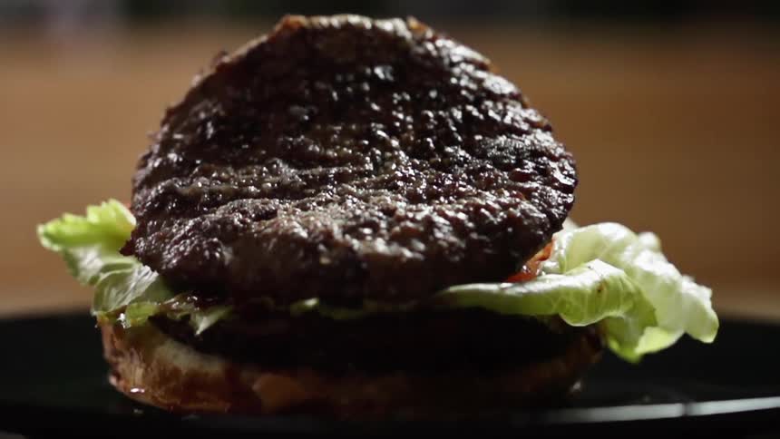 A burger patty falls on a half hamburger bun with lettuce tomato slices and ketchup
