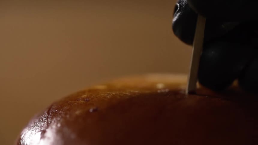 A wood skewer is pushed into a hamburger bun