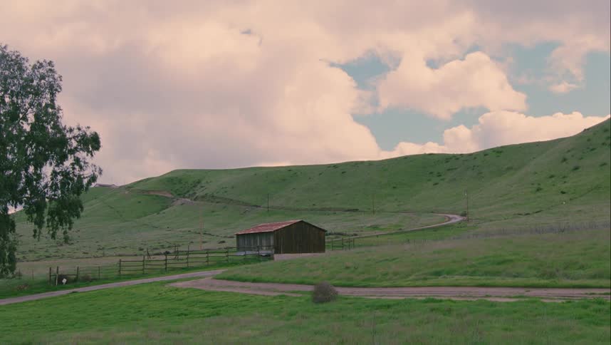 A small vehicle sits in the grass of a large countryside farm
