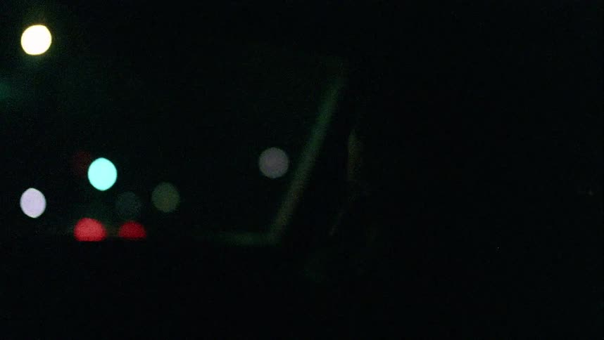 A person sitting in a car with city lights buildings and vehicles outside the car window