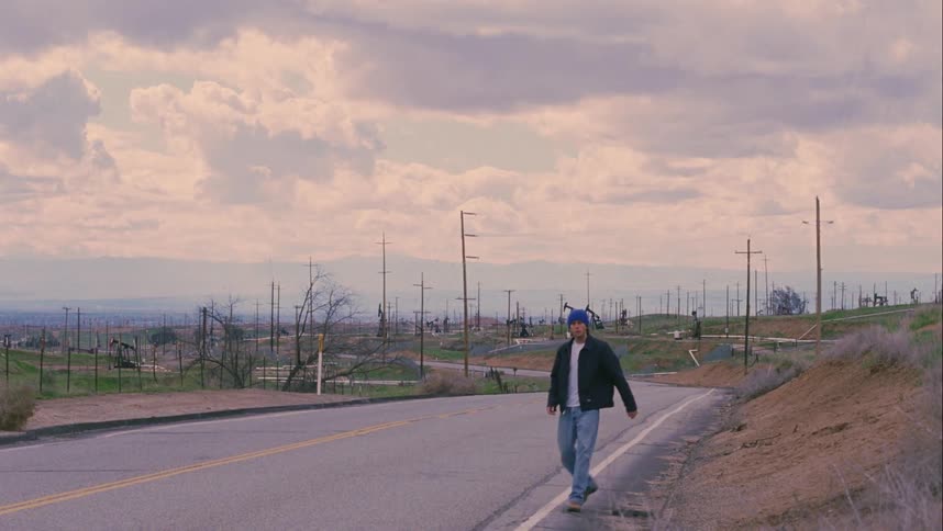 A man walks down the side of the road while constantly looking back over his shoulder