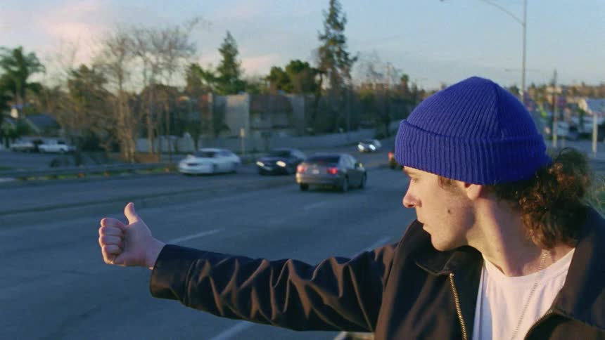 A man sticks his thumb out at passing vehicles to signal that he wants to hitchhike but no vehicle stops for him