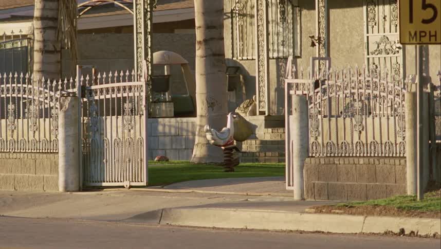 Bag hangs on riding toy bouncing in wind in lawn of home with open gate