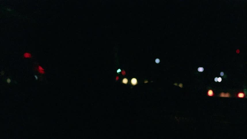 Silhouette of a man driving a car in a small town city street at night