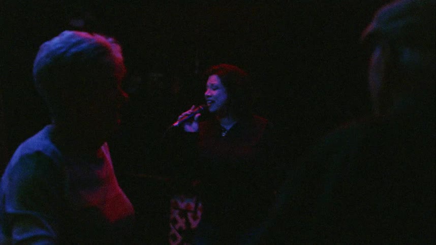 A man and a woman dancing with a woman holding a microphone and singing in the background