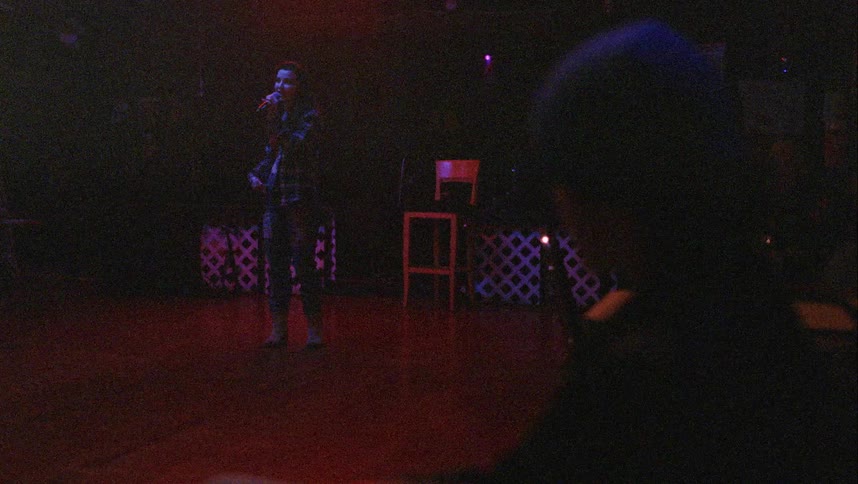 A woman sings in a venue as one person sits and watches and another couple dances