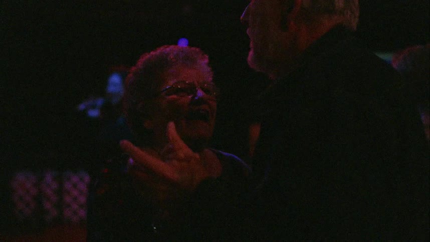 An elderly man and woman dance as another woman sings