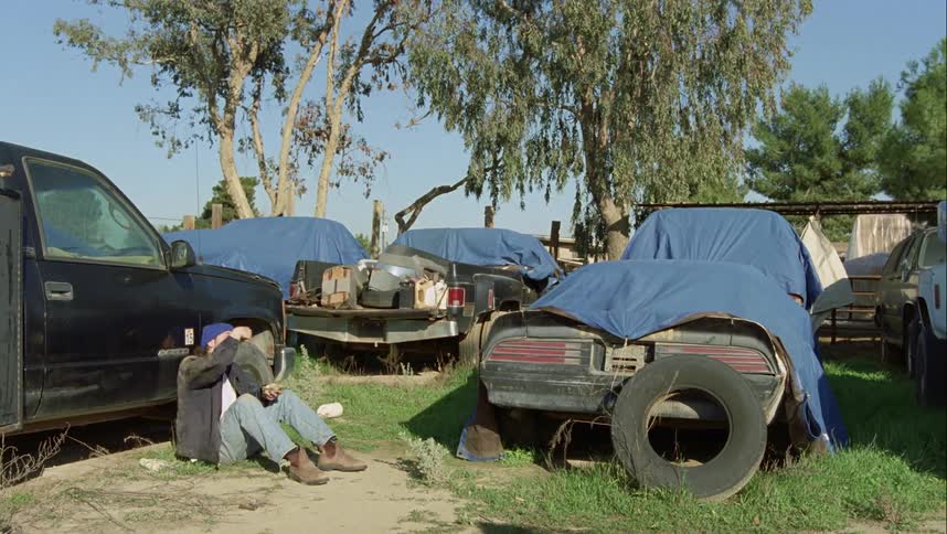 A man sits near a car eating