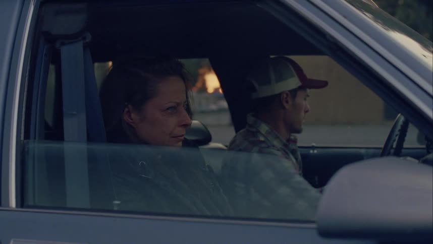 A man driving a car stops and looks over at his wife who is crying and back at his son and then gets out of the car