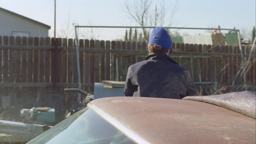 Person wearing blue cap wakes up in junk car shakes self off and leaves junkyard