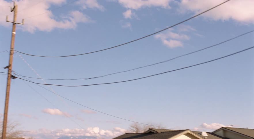 A neighborhood with houses vehicles trees utility poles and the sky in the background
