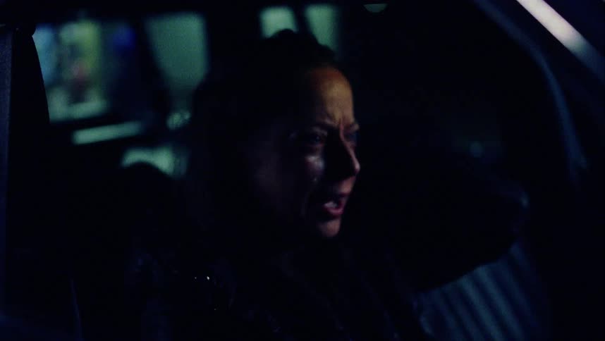 A woman cries while sitting in a dark vehicle at night