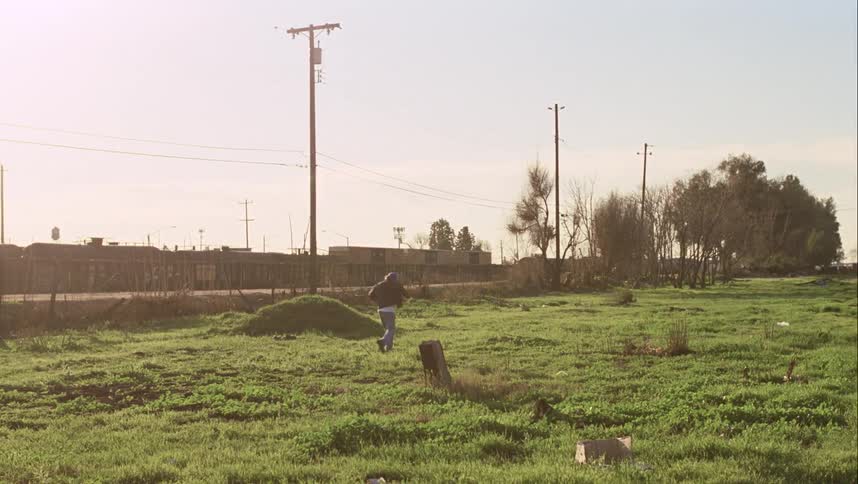 A man with a hat walking on a grassy field with utility poles trees and the sky in the background