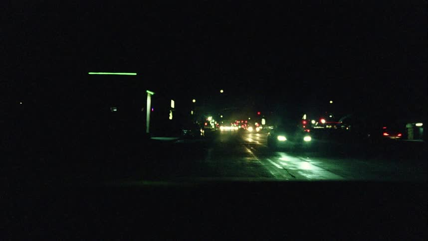 Cars drive along street dotted with lights from business at night