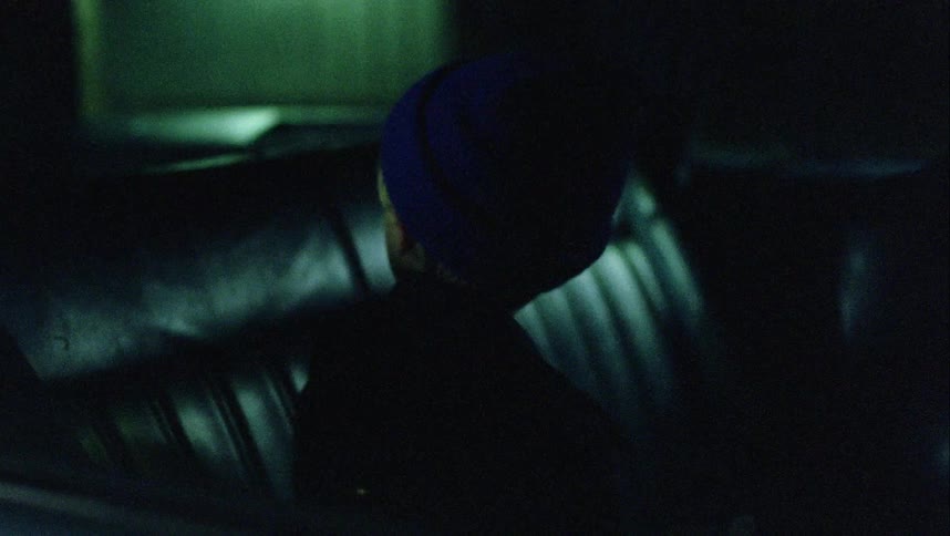 A young boy in a knit beanie sits in the backseat of a car and looks around apprehensively
