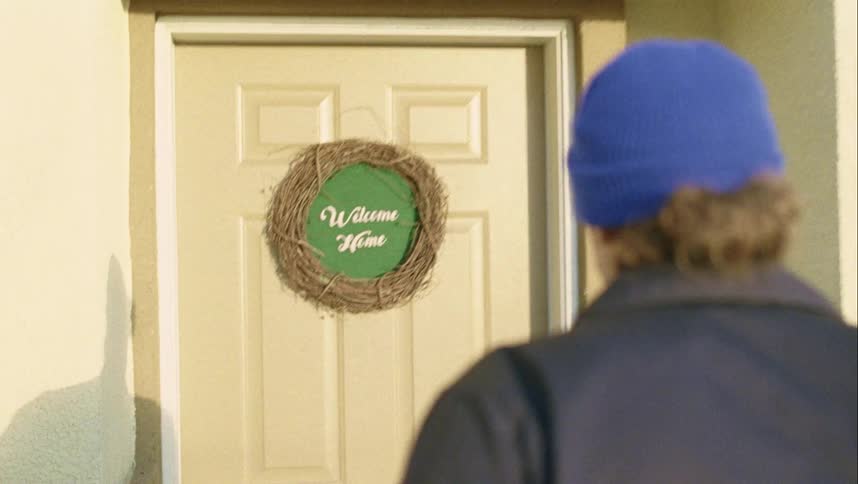 A man with a hat walking up to a house front door
