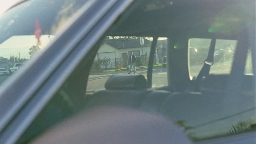 A car sits parked in a neighborhood and a man walking down the street stops and stares at it