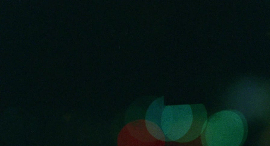 A car air freshener hanging up with the car windshield and city lights in the background