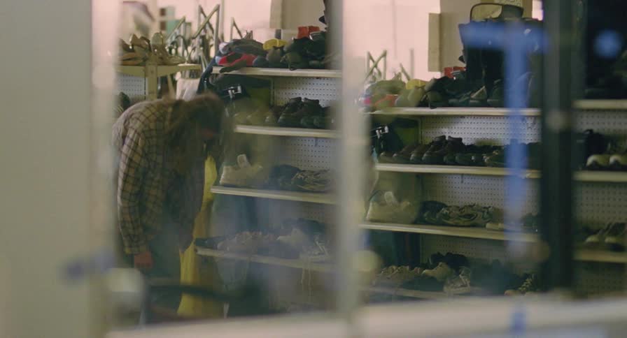 Man puts on shoes at returns merchandise to shelves in shoe store while looking around