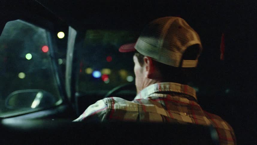 Man gets out of drivers seat after looking over shoulder at child in rear seat near busy street at night