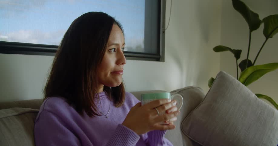 Female sitting on couch gazes to the left while sipping on a cup of coffee