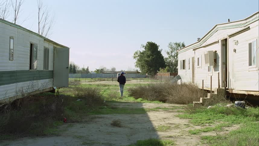 A teenager walks out of a mobile home and across the grass