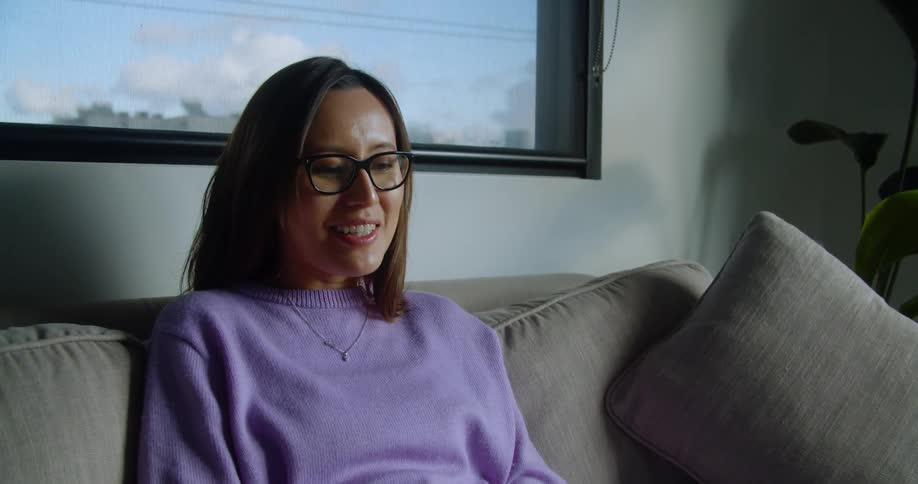 A woman sits on the couch talking and waving