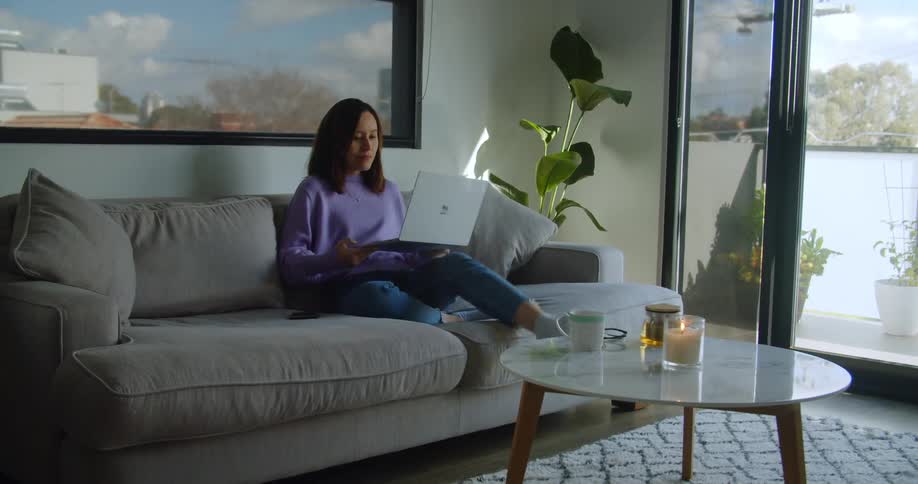 A woman sits on her couch and picks up her laptop