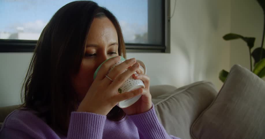 A woman sitting at home drinks a cup of tea