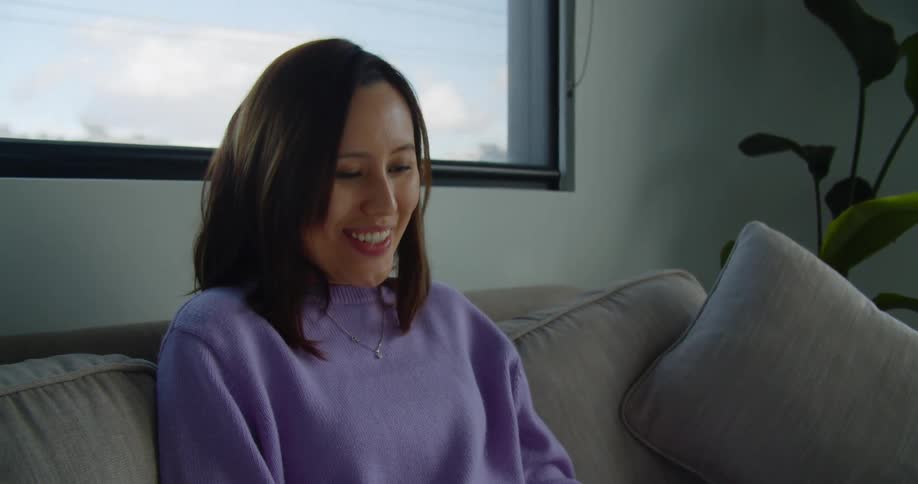 A woman sitting at home types on her laptop and then waves as she video chats with someone